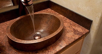 Copper vessel sink with running water on granite countertop