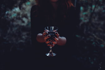 Woman holding dark drink in glass with black nails