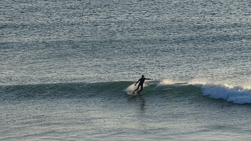 Surfer riding a wave in the ocean at sunset