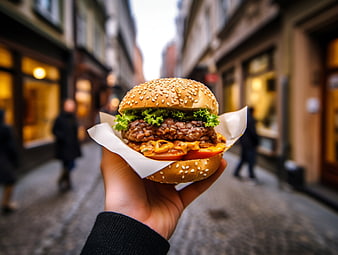 Hand holding delicious burger on city street