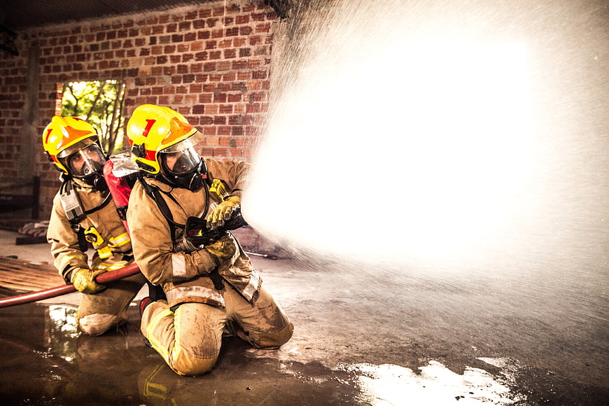 Two Firefighters Kneeling With Water Hose During Training