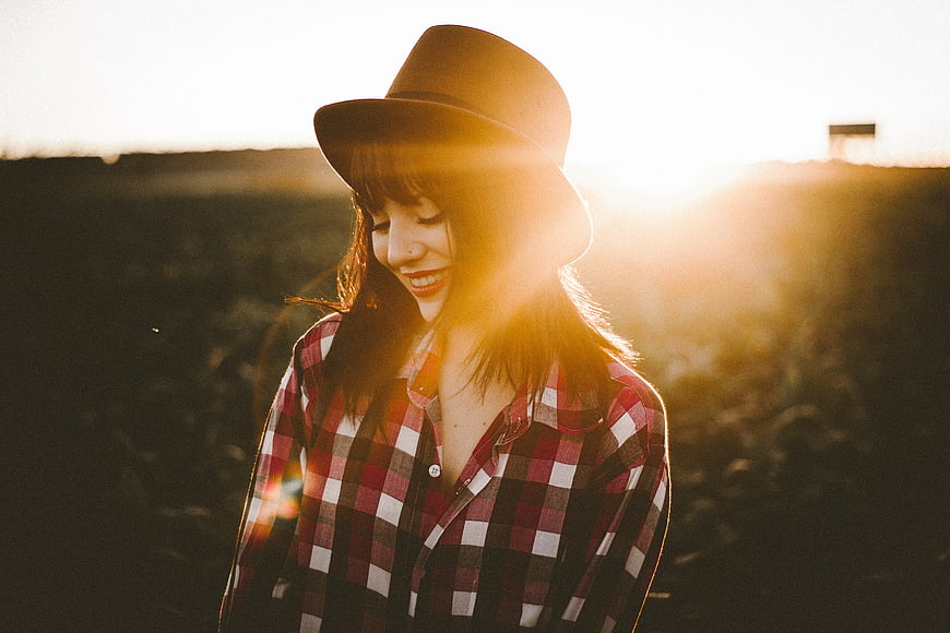 Smiling woman in plaid shirt and hat at sunset