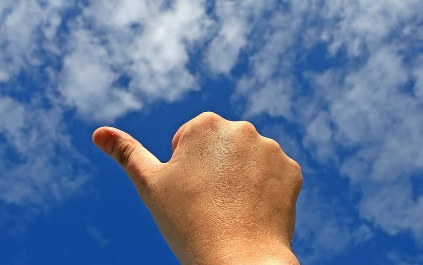 Hand Thumbs Up Gesture Against Blue Sky with Clouds