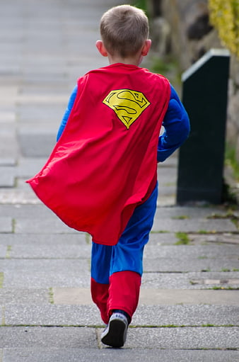 Young Boy Running in Superman Costume on Paved Path