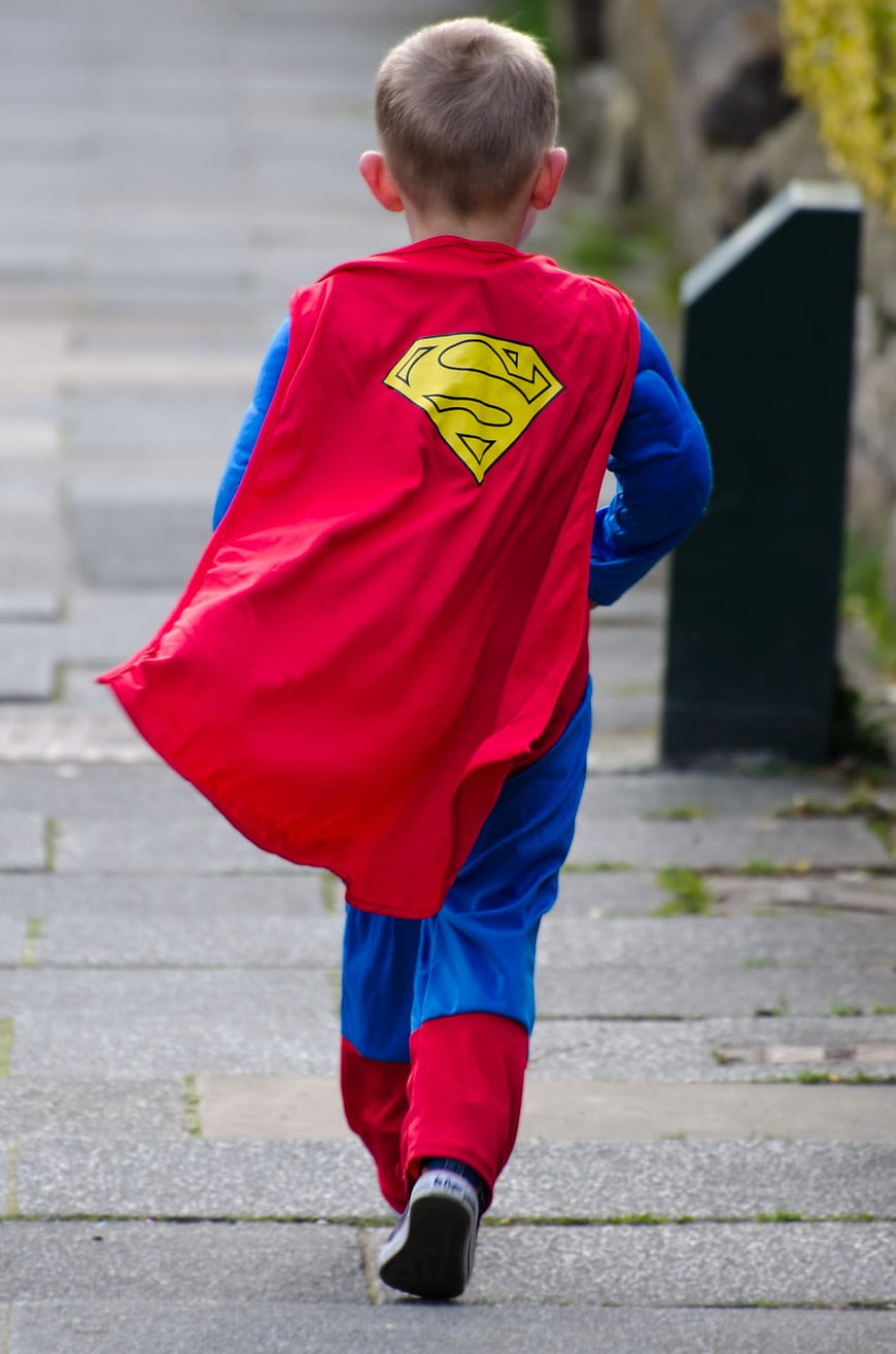 Young Boy Running in Superman Costume on Paved Path