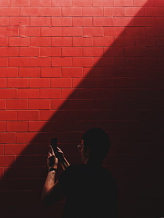 Man Taking Photo Against Red Brick Wall in Shadow