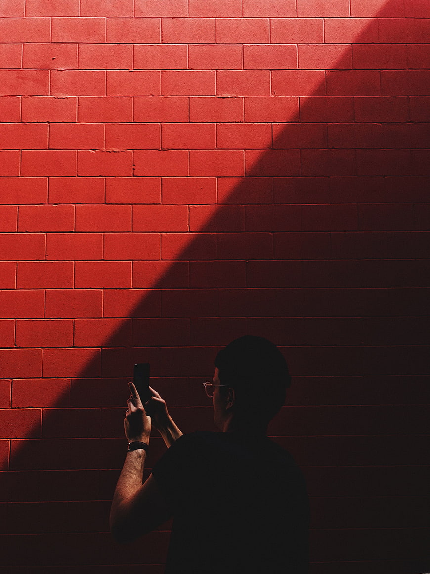 Man Taking Photo Against Red Brick Wall in Shadow