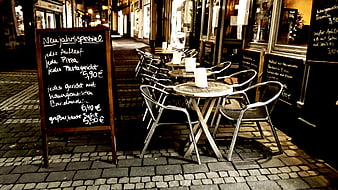 Empty Outdoor Restaurant Seating With Chalkboard Menu On Cobblestone Street At Night