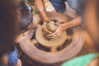 Potter shaping clay on spinning wheel with children watching
