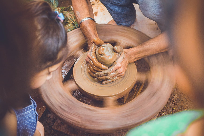 Potter shaping clay on spinning wheel with children watching