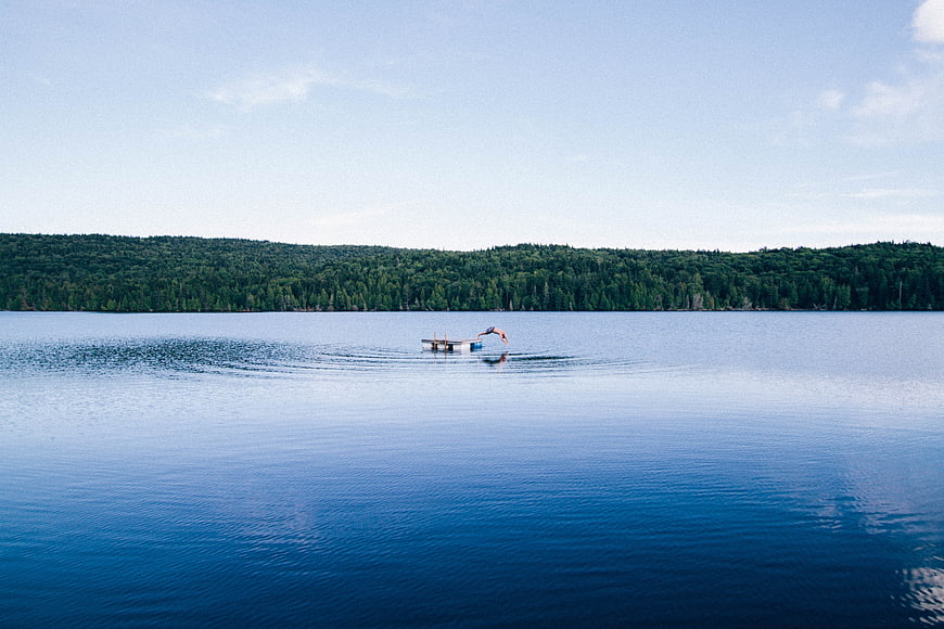 Person diving off dock into serene blue lake