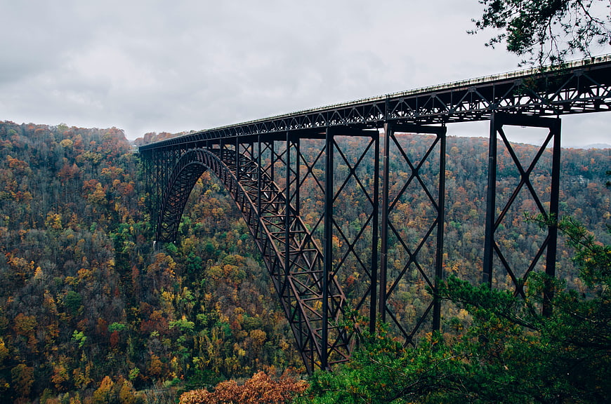 Steel arch bridge spanning autumn forest valley