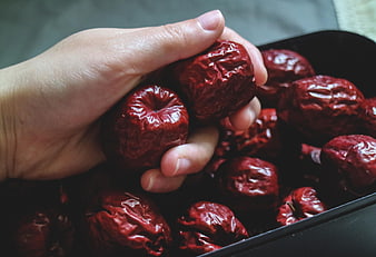 Hand Holding Dried Red Jujubes in Black Bowl