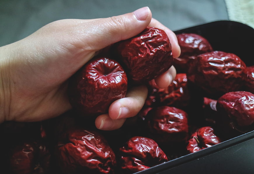 Hand Holding Dried Red Jujubes in Black Bowl