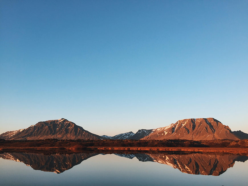 Snow-capped mountains reflected in calm lake at golden hour