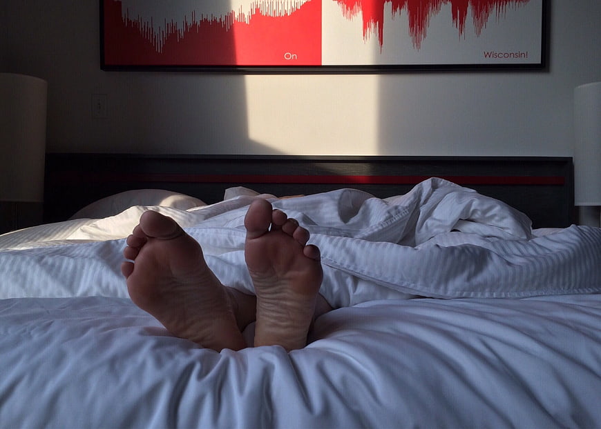 Relaxed bare feet resting on white hotel bed linens