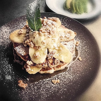 Stack of pancakes with bananas, walnuts, and powdered sugar