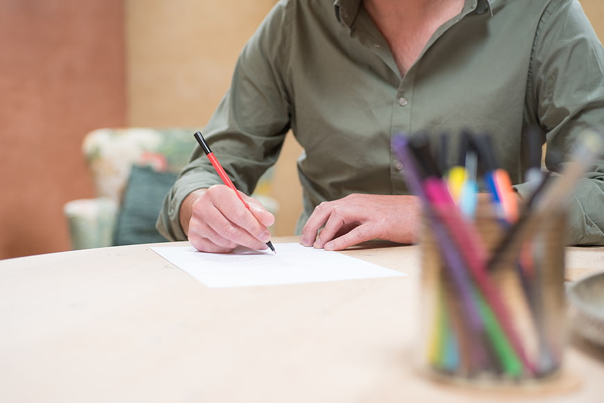 Man writing on paper with red pen at wooden desk