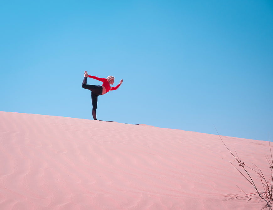 Woman doing yoga on pink sand dune under blue sky