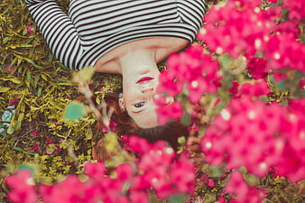 Redhead woman lying in grass surrounded by pink flowers
