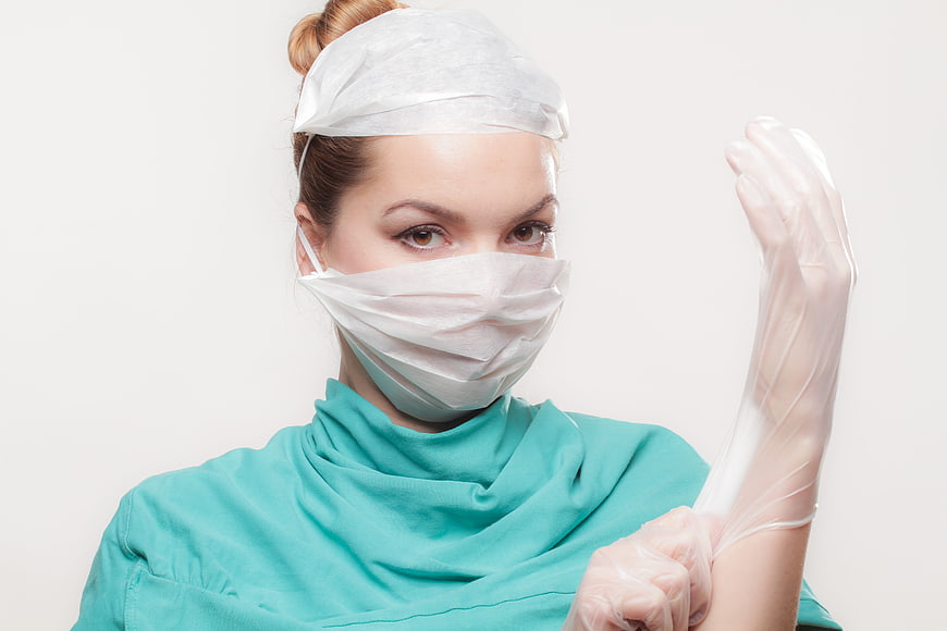 Female surgeon putting on medical gloves in teal scrubs