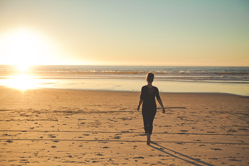 Woman Walking on Sandy Beach at Golden Sunset