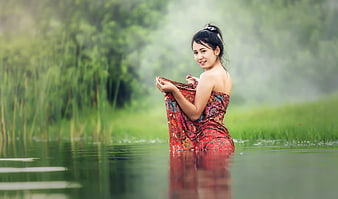 Young woman in traditional red dress standing in a misty green river