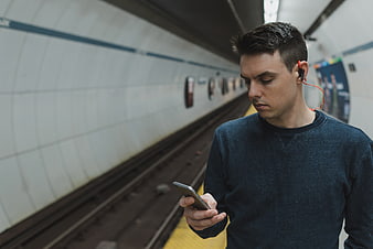Man using smartphone with headphones on subway platform