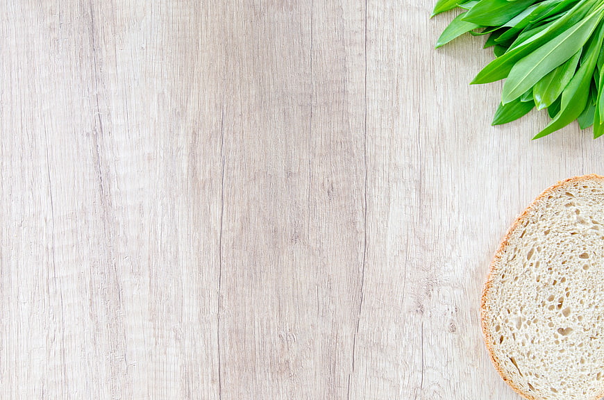 Fresh wild garlic leaves and bread slice on light wood background