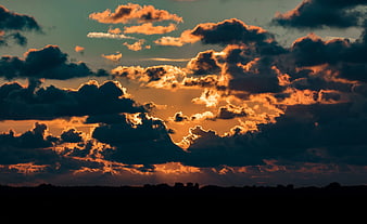 Dramatic sunset with golden sun rays breaking through dark clouds