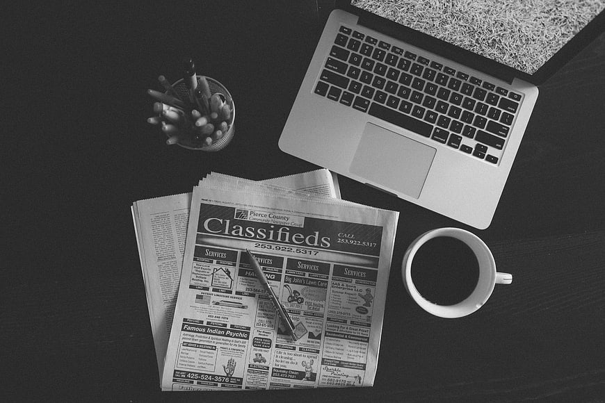 Black and white flat lay of laptop, newspaper, and coffee