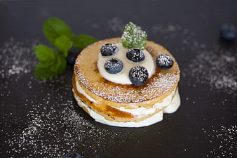 Stack of blueberry pancakes with cream and mint on dark background