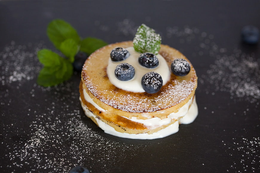 Stack of blueberry pancakes with cream and mint on dark background