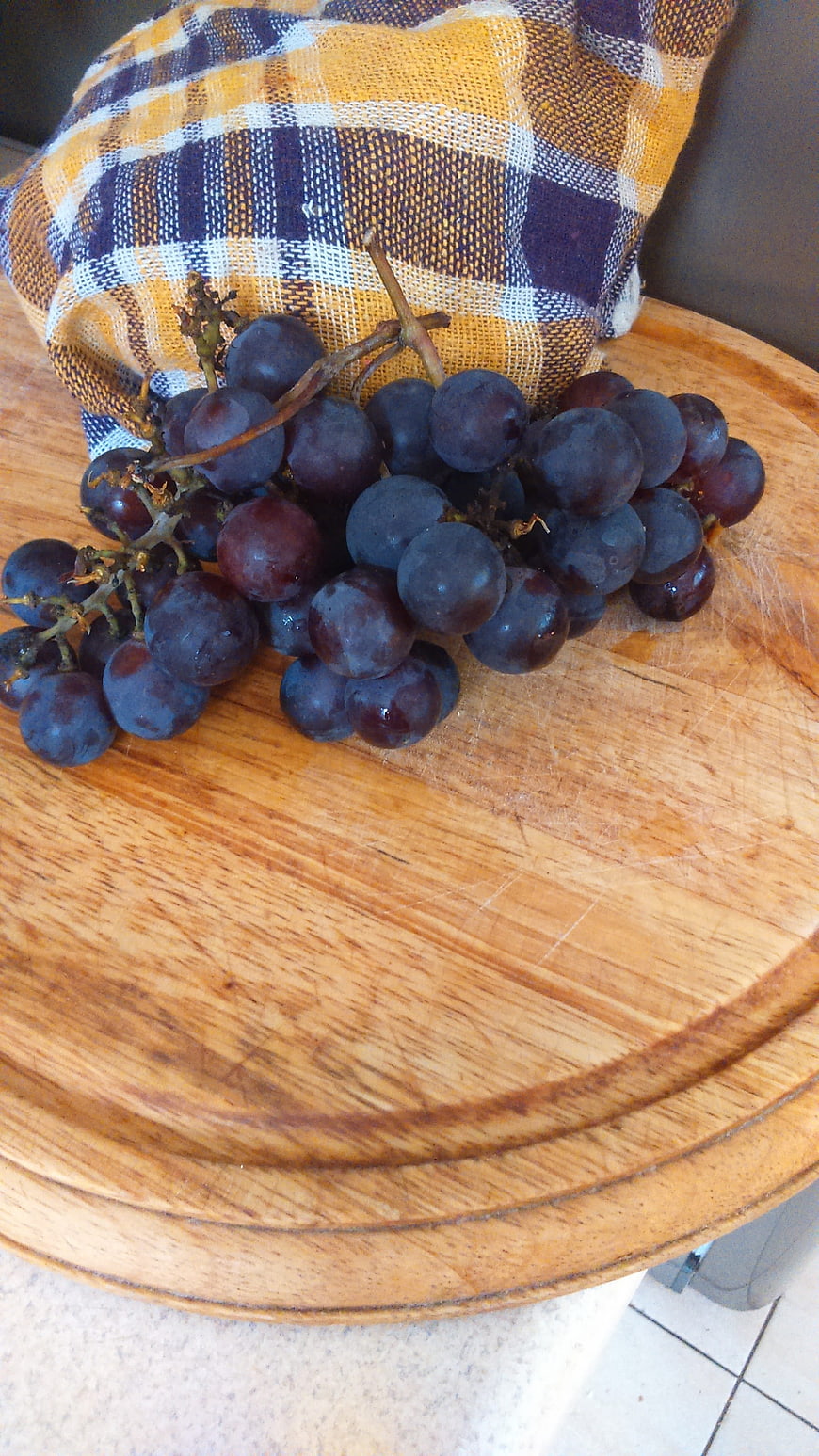 Fresh purple grapes on a wooden cutting board with checkered cloth