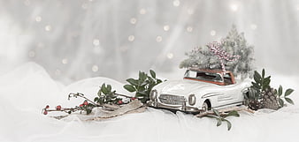 Vintage white toy car carrying Christmas tree on snowy background