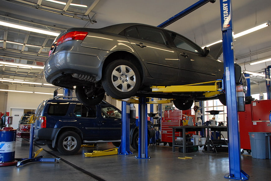 Gray sedan elevated on hydraulic lift in professional auto repair shop