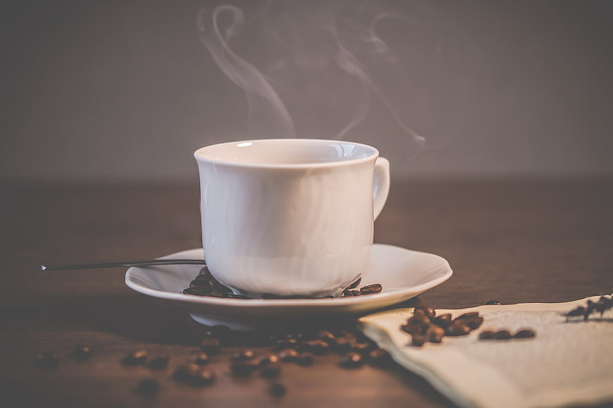 Steaming White Coffee Cup with Beans on Wooden Table