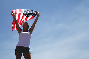 Woman holding American flag against blue sky