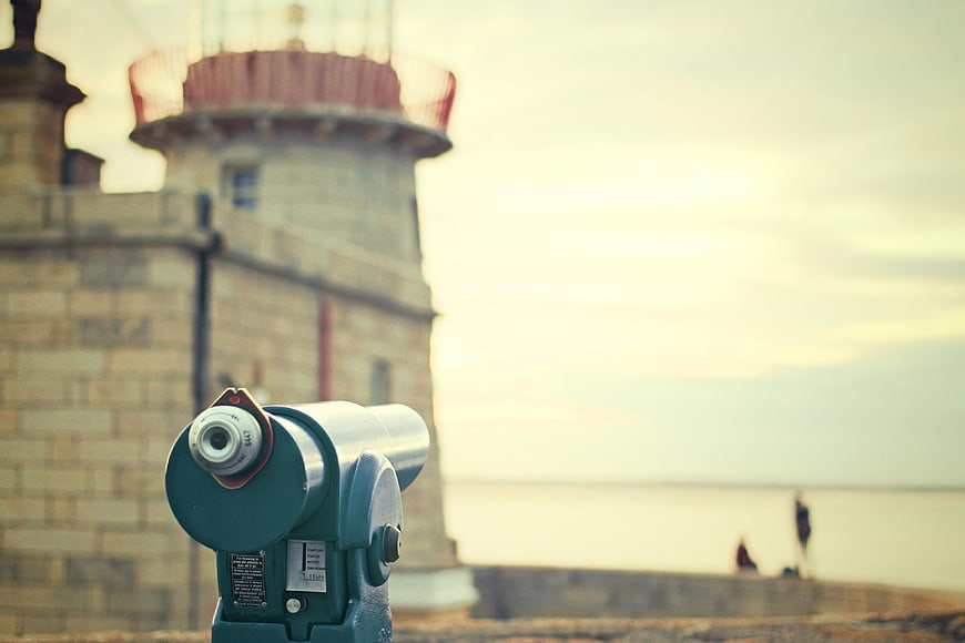 Green coin-operated binoculars with blurred lighthouse background