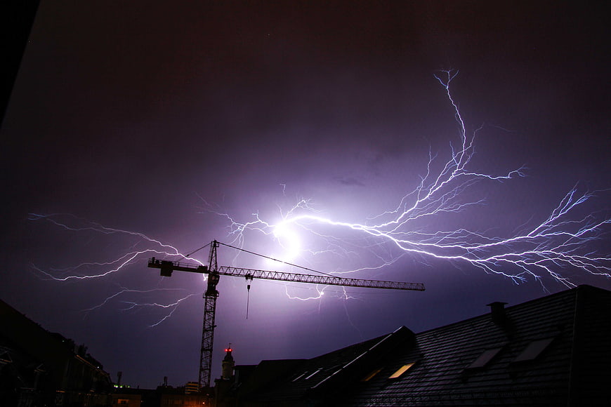 Dramatic lightning strike over construction crane and city rooftops at night
