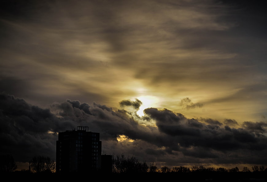 Dramatic sunset with sun breaking through dark clouds over city silhouette