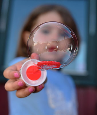 Child Blowing Soap Bubble with Red Wand Close Up