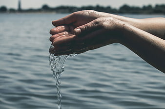 Close-up of hands pouring water over a lake background