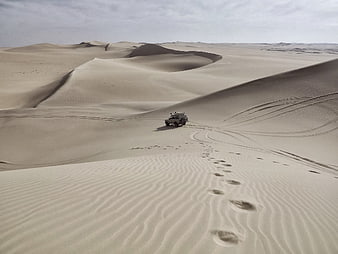 Off-road SUV driving through vast desert sand dunes with footprints
