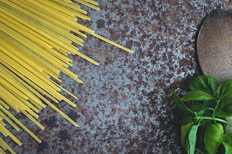 Uncooked spaghetti, fresh basil, and wooden spoon on rustic metal background