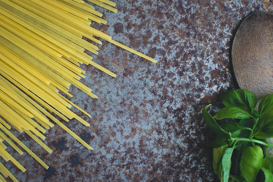 Uncooked spaghetti, fresh basil, and wooden spoon on rustic metal background