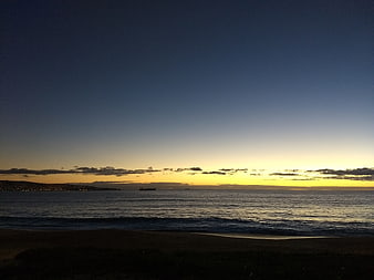 Serene Sunset Over Ocean with Distant Ship and Coastal Lights