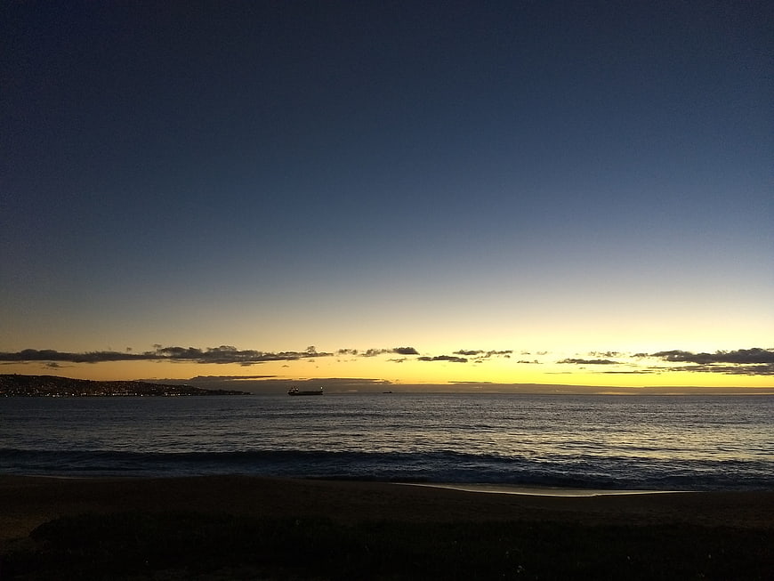 Serene Sunset Over Ocean with Distant Ship and Coastal Lights