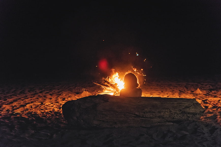 Woman Silhouette Sitting By Campfire On Beach At Night