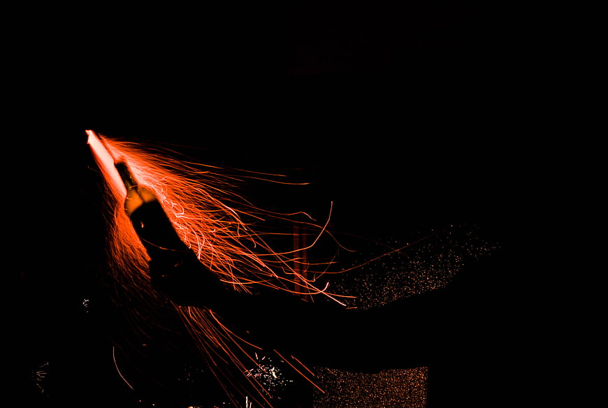 Hand holding glowing sparkler with flying sparks in the dark